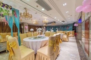Un salón de banquetes con mesas redondas, sillas y una araña.