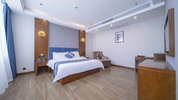 A hotel room with a bed, a desk, a chair, and a desk lamp.