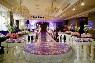 Un salón de banquetes con una larga mesa dispuesta para un evento formal, flanqueado por columnas blancas y arreglos florales.