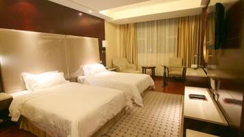 A hotel room with two beds, a desk, a chair, and a TV.