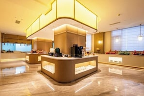 Un hall d’hôtel moderne avec un comptoir d’accueil central, un espace salon et une grande fenêtre offrant une vue.