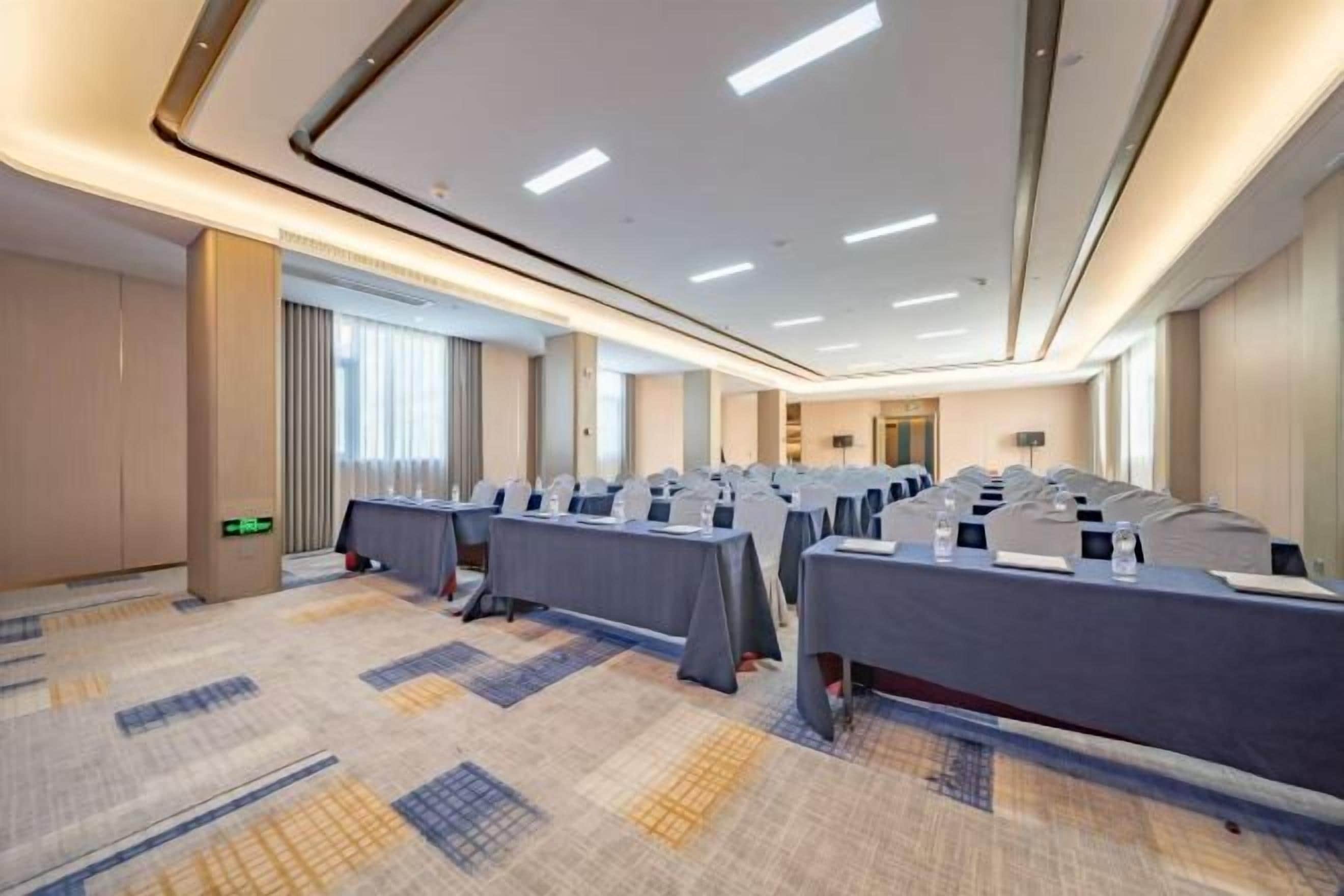 A conference room with rows of tables, a carpeted floor, and a modern ceiling design.