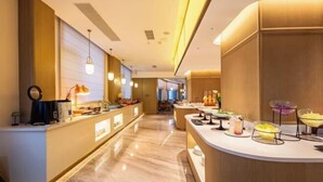 Un moderno vestíbulo de hotel con mostrador de recepción, zona de estar y bufé con diversas opciones de comida.