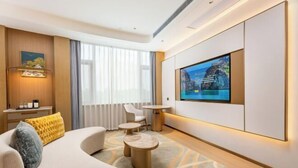 Una habitación de hotel moderna con un televisor de pantalla plana grande, un sofá, una mesita y una lámpara decorativa.