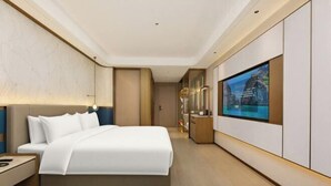 Una habitación de hotel moderna con una cama grande, un televisor en la pared y un pasillo que conduce a un baño.
