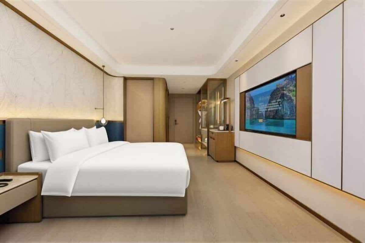 Ein modernes Hotelzimmer mit einem großen Bett, einem Wandfernseher und einem Flur, der zu einem Badezimmer führt.
