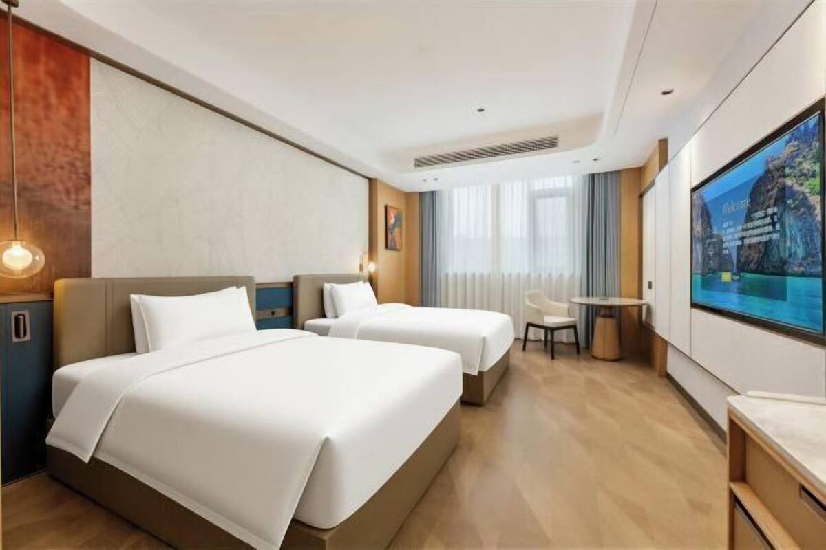 Ein Hotelzimmer mit zwei Betten, einem Schreibtisch, einem Sessel, einem Fernseher und einem großen Fenster.