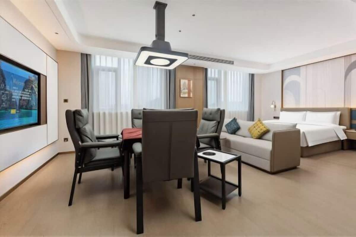 Ein Hotelzimmer mit einem Bett, einem Sofa, einem Esstisch mit Stühlen, einem Fernseher und einer Deckenleuchte.