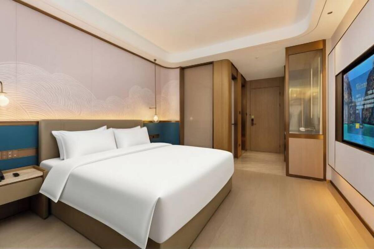 Ein modernes Hotelzimmer mit einem großen Bett, einem Nachttisch, einem an der Wand befestigten Fernseher und einem Schiebetürenschrank.
