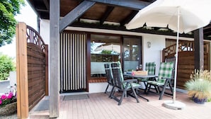 An outdoor patio with a table and chairs, a wooden gate, and a potted plant. - Apartment No.1 - Baltic Sea Crab - Ferienhof Kluvetasch (Neustadt in Holstein)