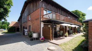 A two-story building with a covered patio area, a brick facade, and a wooden balcony. - Apartment No.1 - Baltic Sea Crab - Ferienhof Kluvetasch (Neustadt in Holstein)