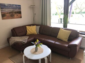 A living room with a brown leather sofa, a white coffee table, and a painting of a beach scene.
