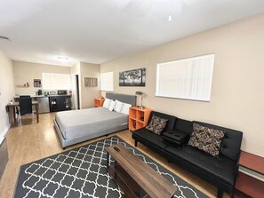 A compact hotel room with a bed, a sofa, a desk, and a kitchenette.