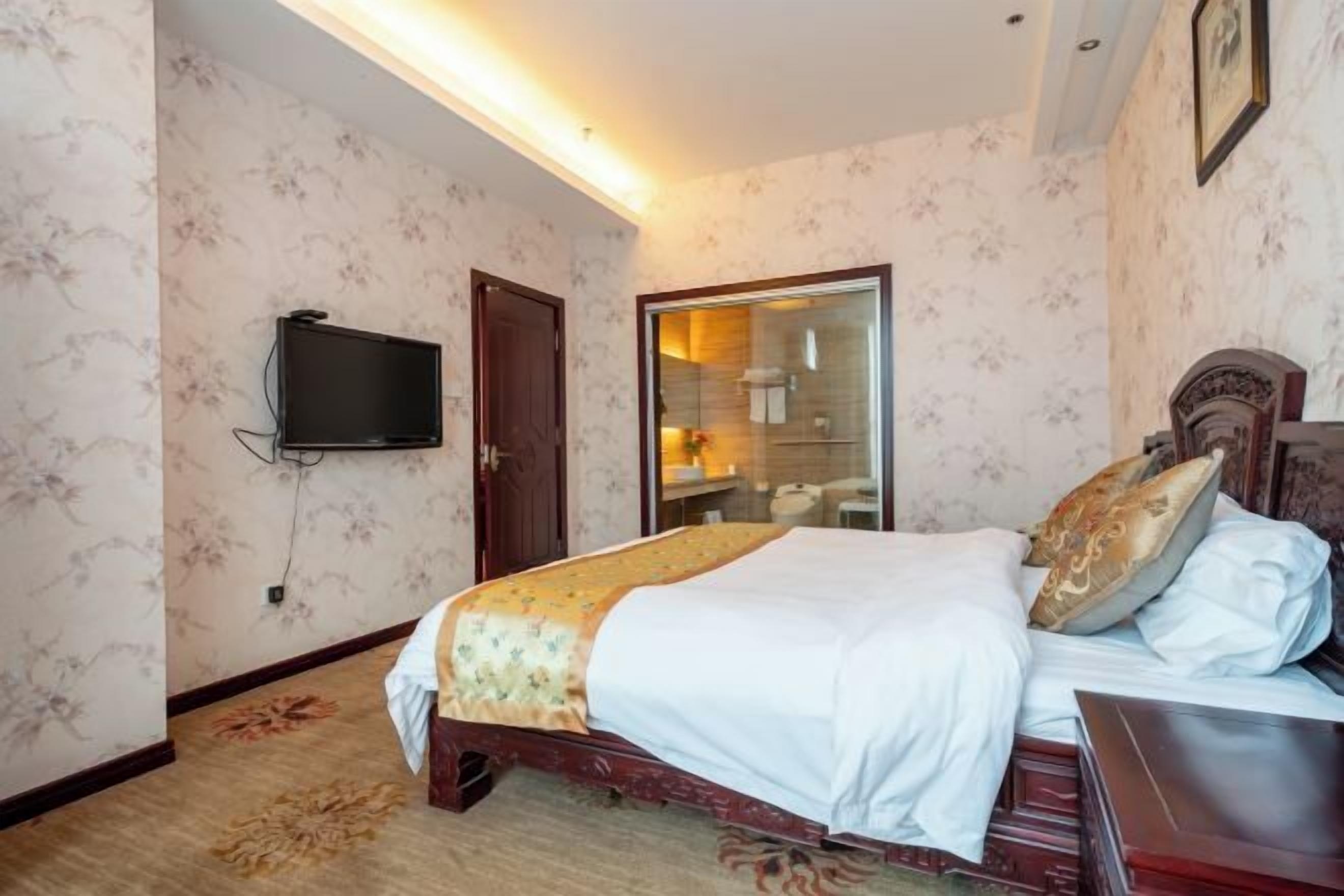 A hotel room with a bed, a television mounted on the wall, and a door leading to a bathroom.