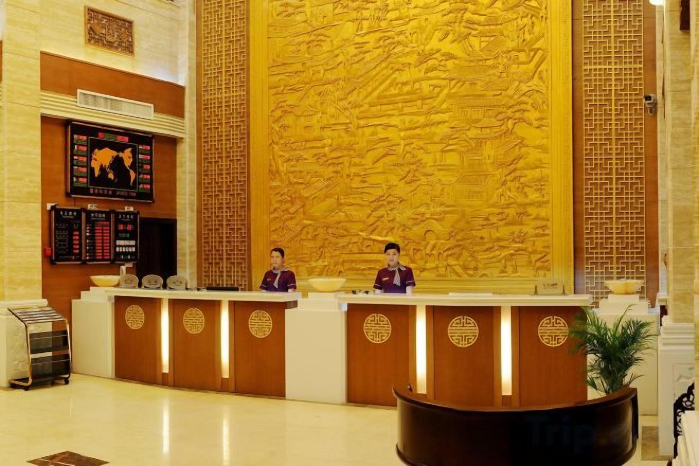Ein Hotel-Empfangsbereich mit einer großen, aufwendig geschnitzten Wand, einem Empfangstisch und einer digitalen Anzeige.