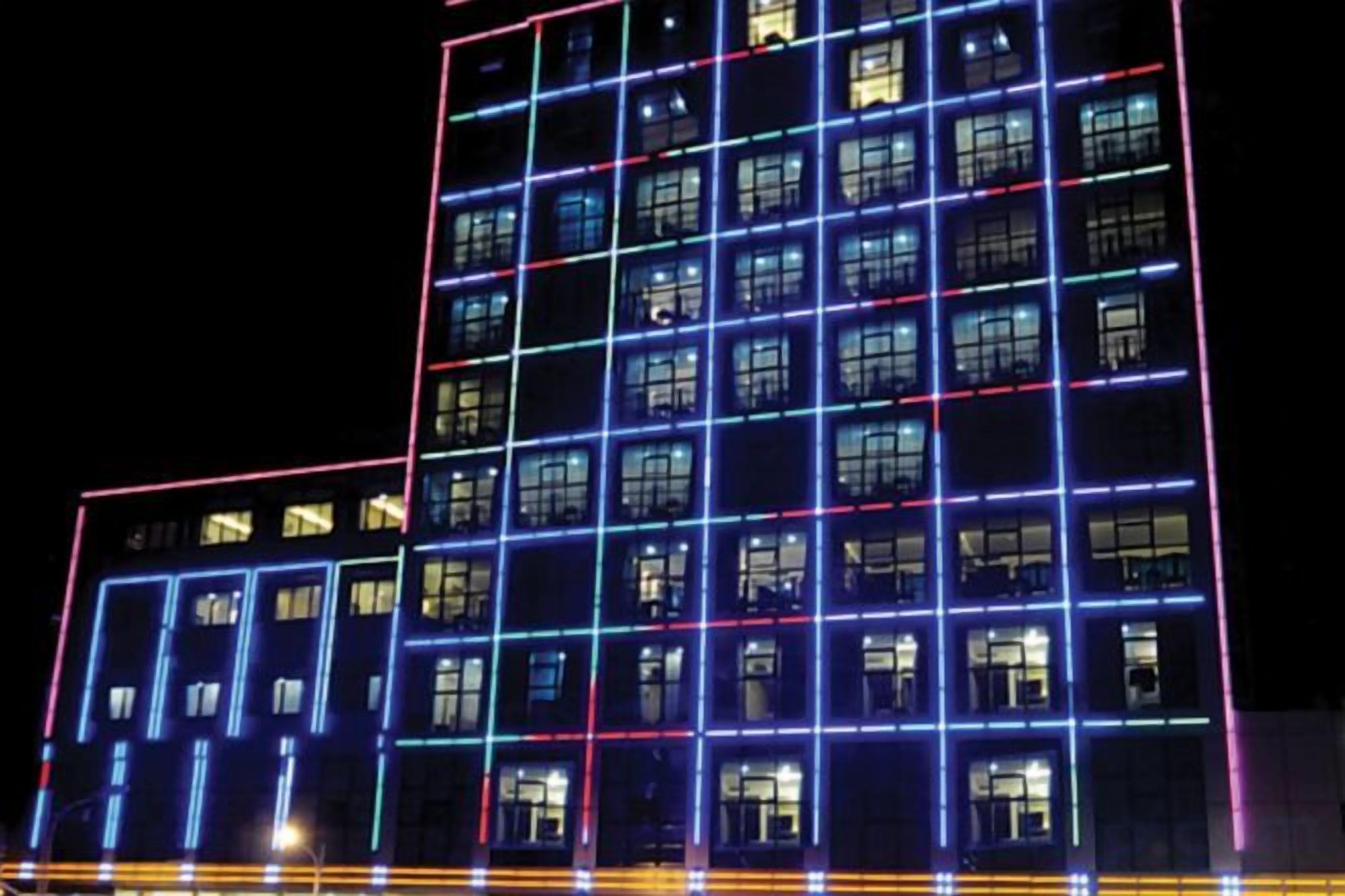 Ein mehrgeschossiges Gebäude mit beleuchteten Fensterkonturen und einer rasterartigen Fassade.
