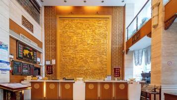 A reception area with a large wall of intricate carvings, a reception desk, and a digital information board.