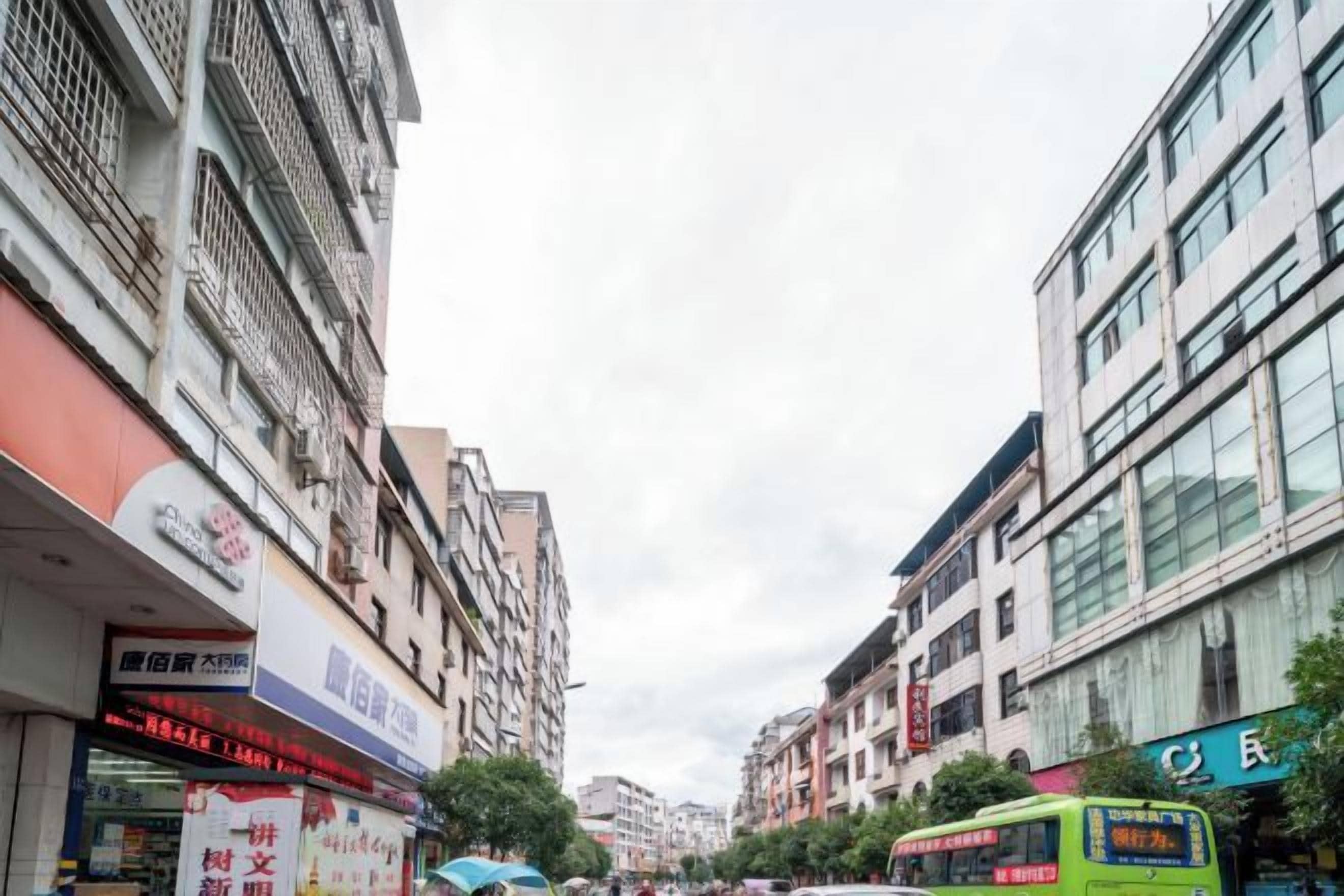 A street with multi-story buildings, a green bus, and various storefronts.