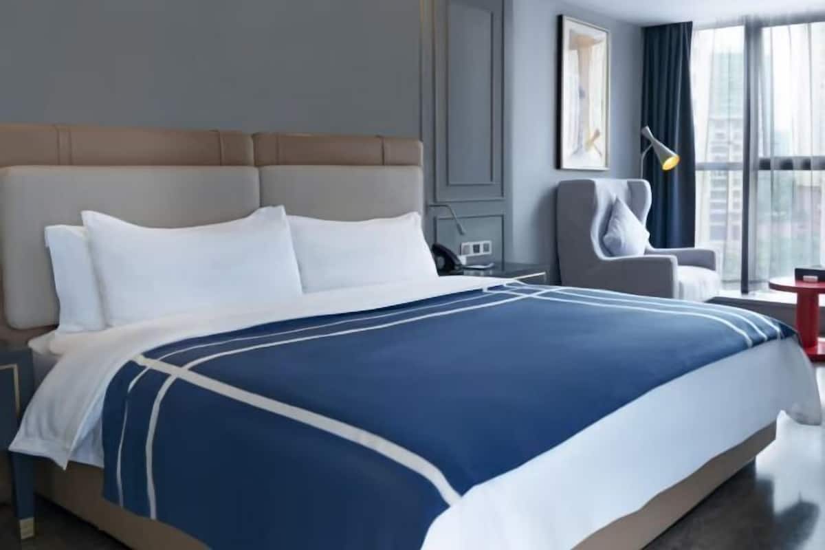 Habitación de hotel con una cama grande, una silla, un escritorio y una ventana con cortinas.
