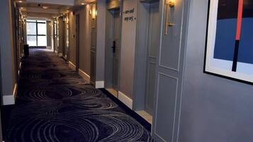 Un couloir d’hôtel avec un tapis à motifs, des portes portant les numéros de chambre et un tableau encadré accroché au mur.