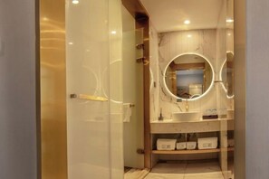 A modern bathroom with a glass door, marble walls, a round mirror, and a vanity with shelves. - Yicheng Hotel (Dafang)