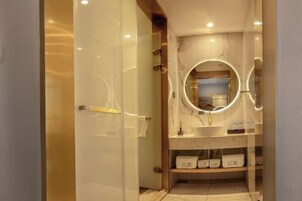 A modern bathroom with a glass door, marble walls, a round mirror, and a vanity with shelves.