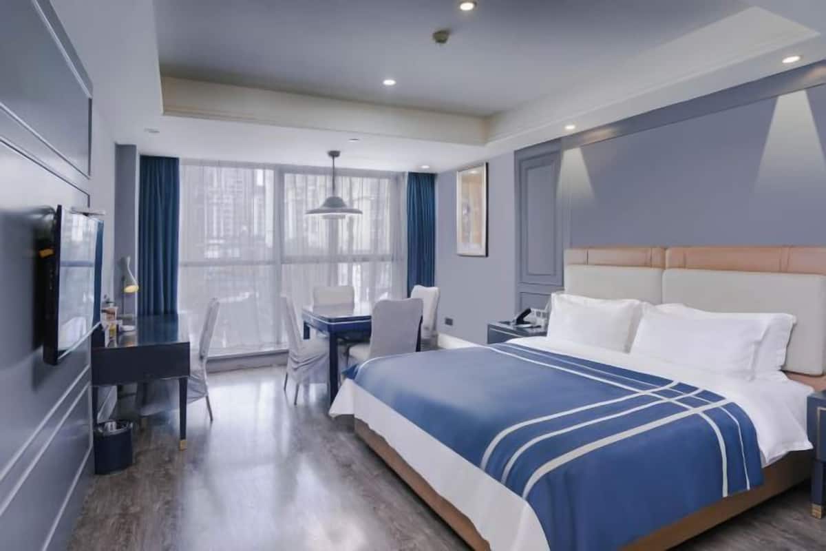 Habitación de hotel con cama, escritorio, silla y un amplio ventanal.
