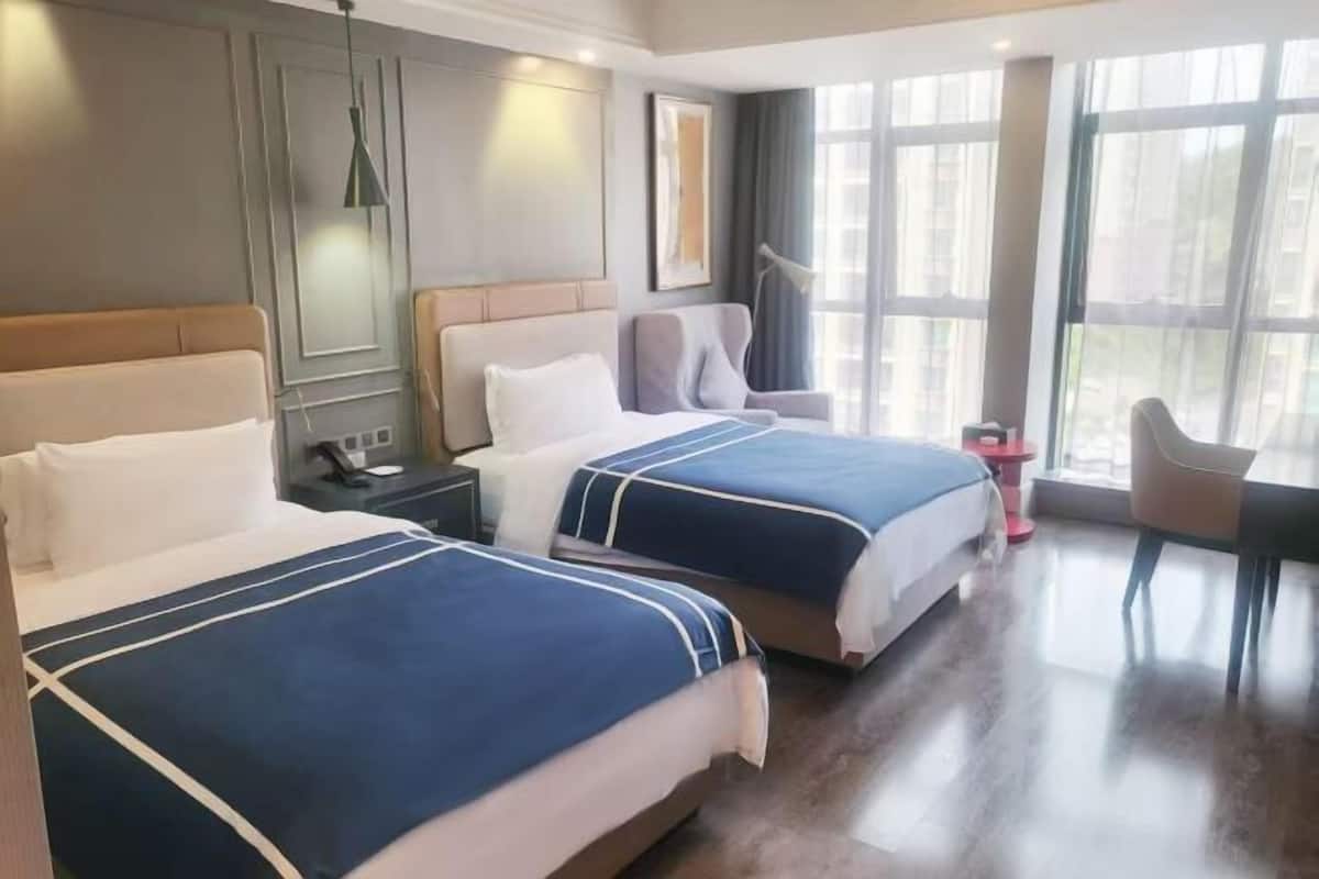 Habitación de hotel con dos camas, un escritorio, una silla y ventanas amplias.