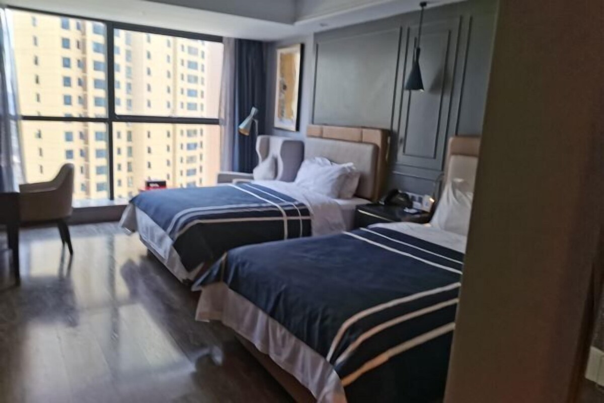 Habitación de hotel con dos camas, un escritorio y vistas a edificios altos.