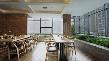 A modern dining area with long tables and chairs, large windows, and a brick wall.