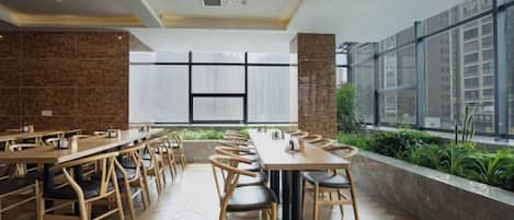 Un comedor moderno con mesas largas, sillas, ventanas amplias y una pared de ladrillo.