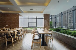 Un comedor moderno con mesas largas, sillas, ventanas amplias y una pared de ladrillo.