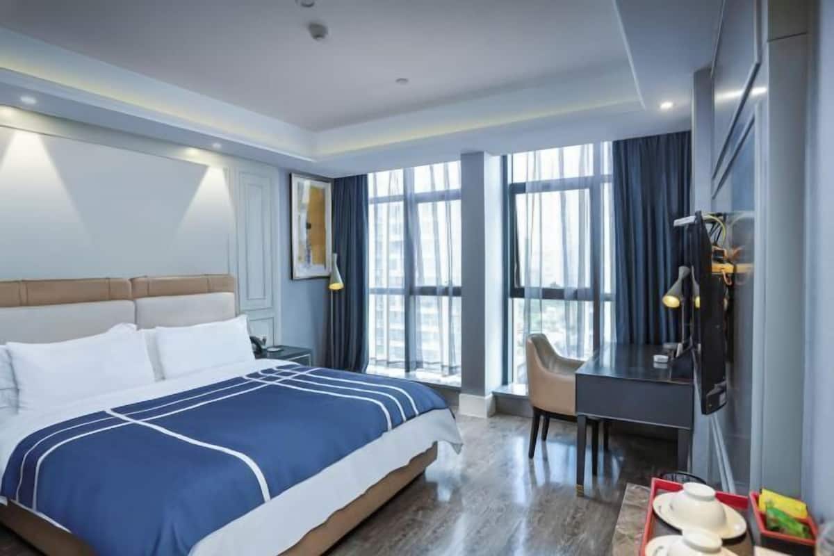 Una habitación de hotel con una cama, un escritorio, un televisor y ventanas grandes.