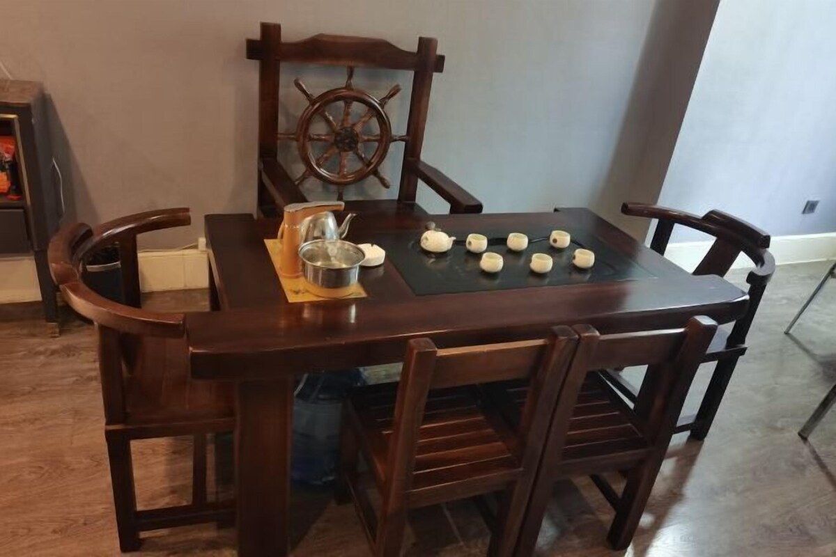 Una mesa de comedor de madera con cuatro sillas, un adorno de timón de barco y varios objetos pequeños de cerámica sobre la mesa.