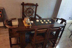 A wooden dining table with four chairs, a ship's wheel decoration, and several small ceramic objects on the table.