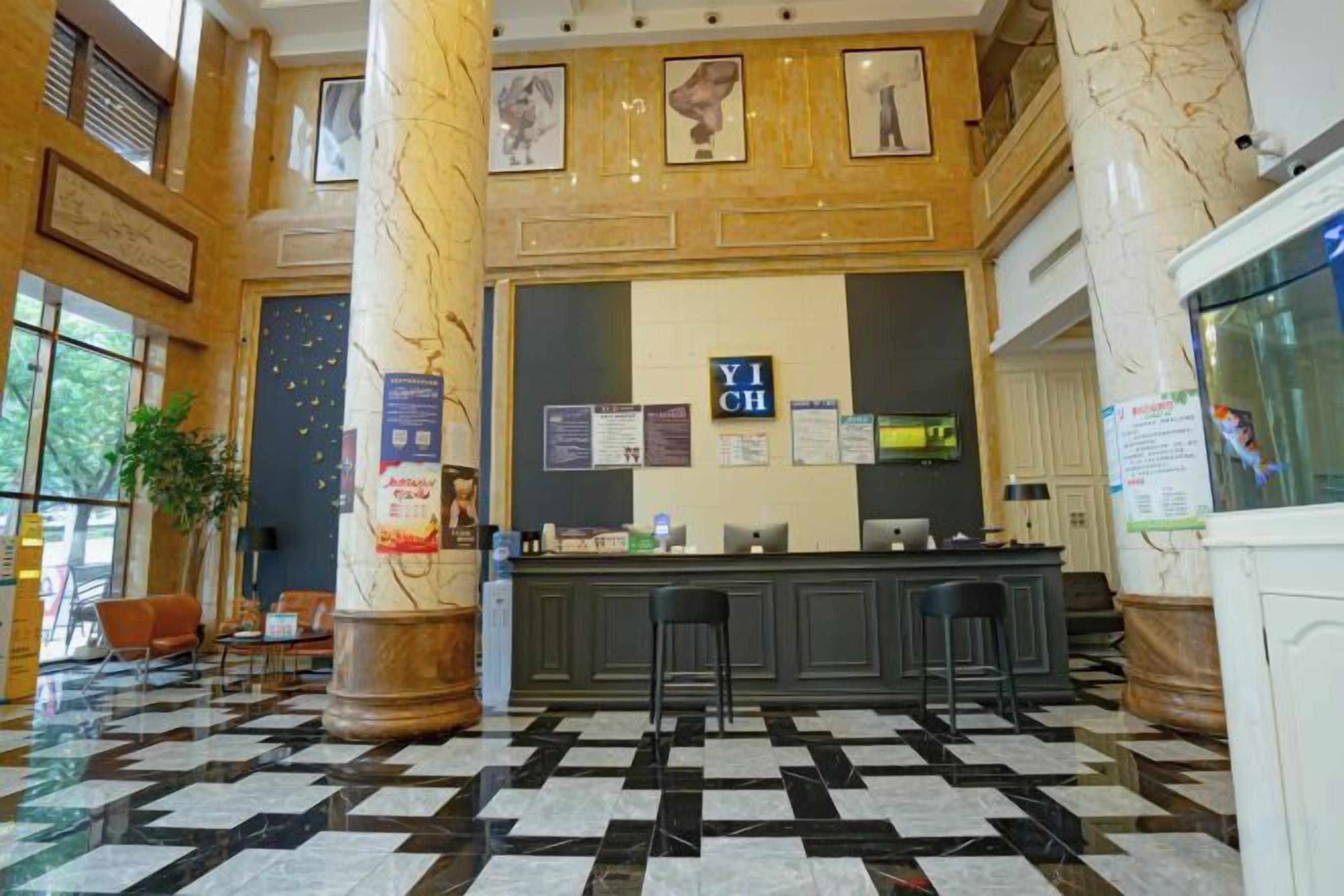 Un hall con mostrador de recepción, mostradores de registro y de salida. Hay sillas y una planta en maceta.