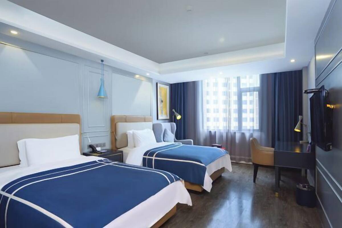 Habitación de hotel con dos camas, un escritorio, una silla, un televisor y una ventana con cortinas.