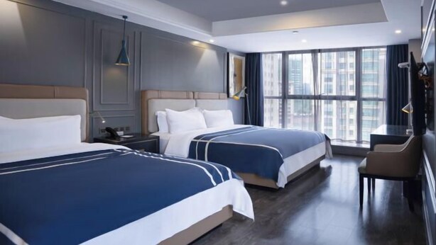 Una habitación de hotel con dos camas, un escritorio, una silla y ventanas amplias.