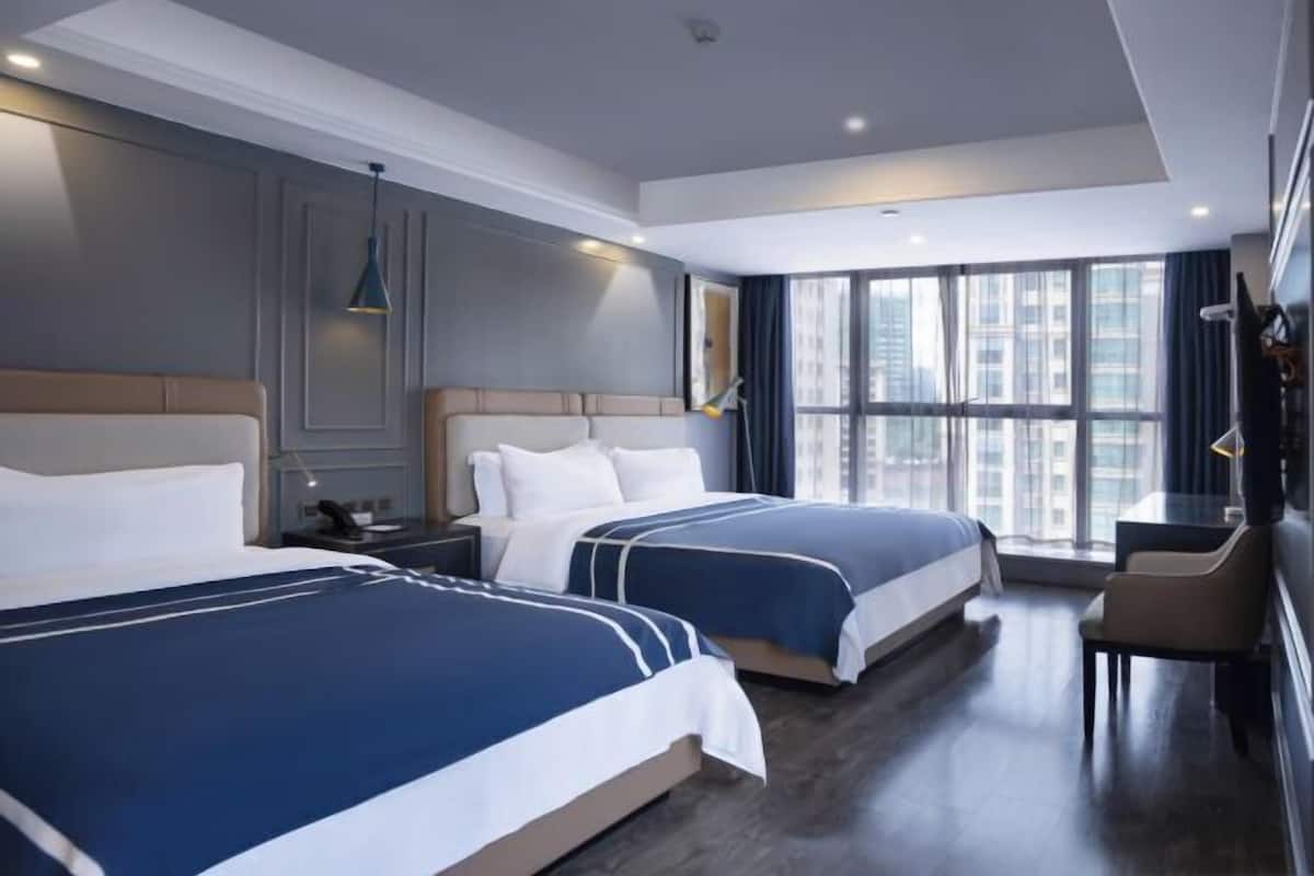Una habitación de hotel con dos camas, un escritorio, una silla y ventanas amplias.