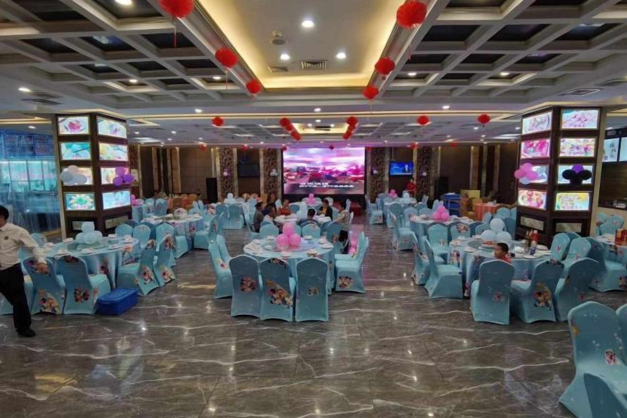 A banquet hall with round tables, chairs, and a stage with a screen.