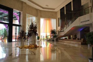 A spacious lobby with a high ceiling, a staircase, and a large window with a view of the outdoors. - Beiliu International Hotel (Beiliu)