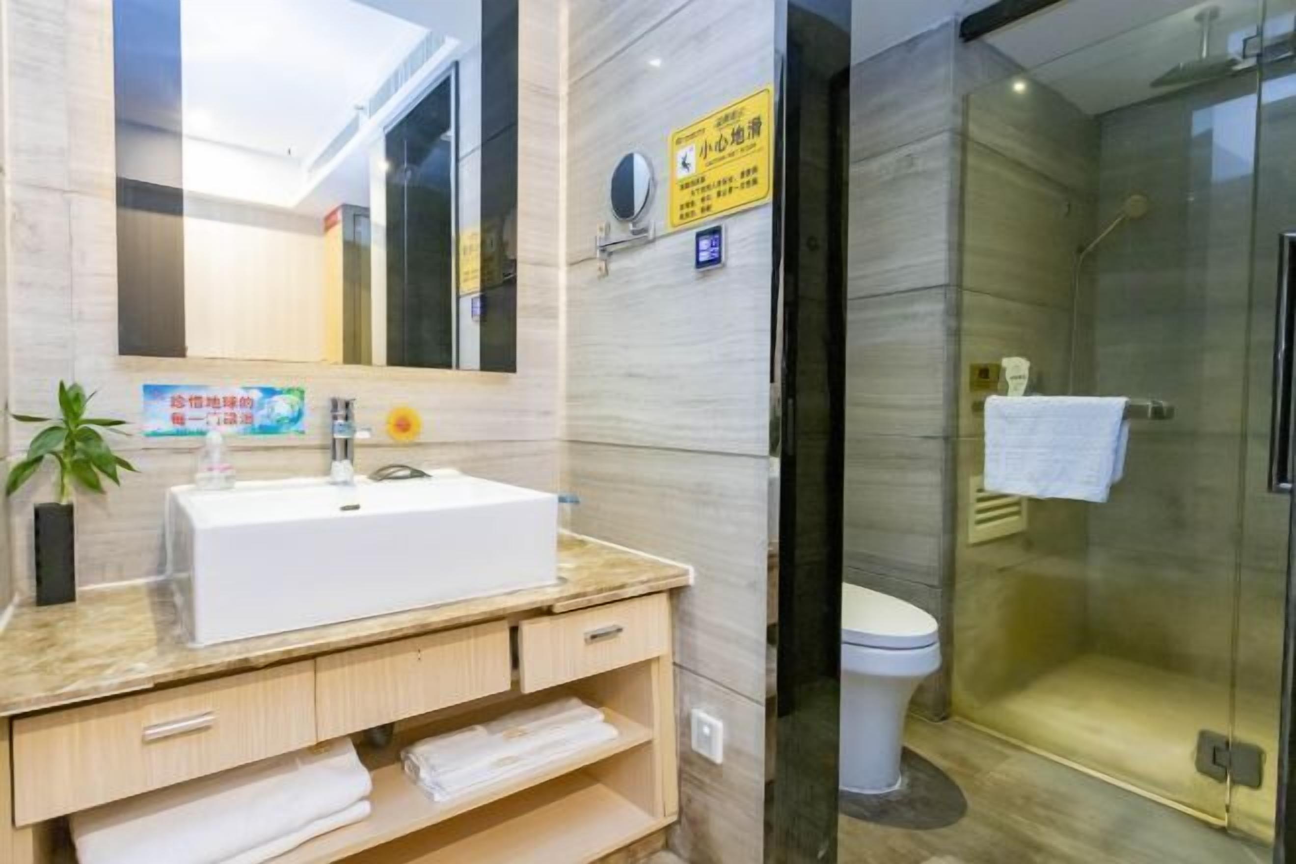A modern bathroom with a white sink, a mirror, a glass shower enclosure, and a sign on the wall.