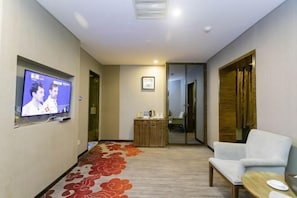 A hotel room with a television on the wall, a seating area with a chair and table, and a carpeted floor. - Beiliu International Hotel (Beiliu)