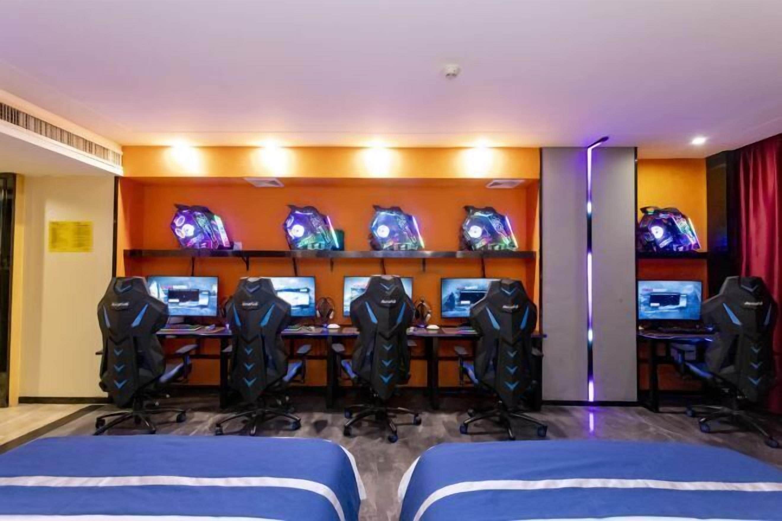 Ein Gaming-Raum mit mehreren Gaming-Stationen, ausgestattet mit je einem Bildschirm und einem Gaming-Sessel. Im Vordergrund befinden sich zwei Betten.