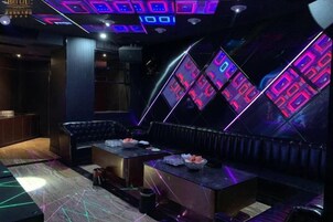 Una habitación con poca luz, que incluye una zona de bar, un área de estar con mesas y una pared con pantallas iluminadas.
