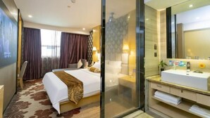 A hotel room with a large bed, a glass partition, a bathroom with a white sink, and a large mirror. - Beiliu International Hotel (Beiliu)