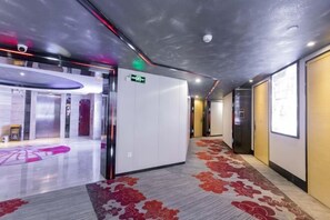 A hotel corridor with a patterned carpet, a reception area with a glass partition, and a modern elevator. - Beiliu International Hotel (Beiliu)