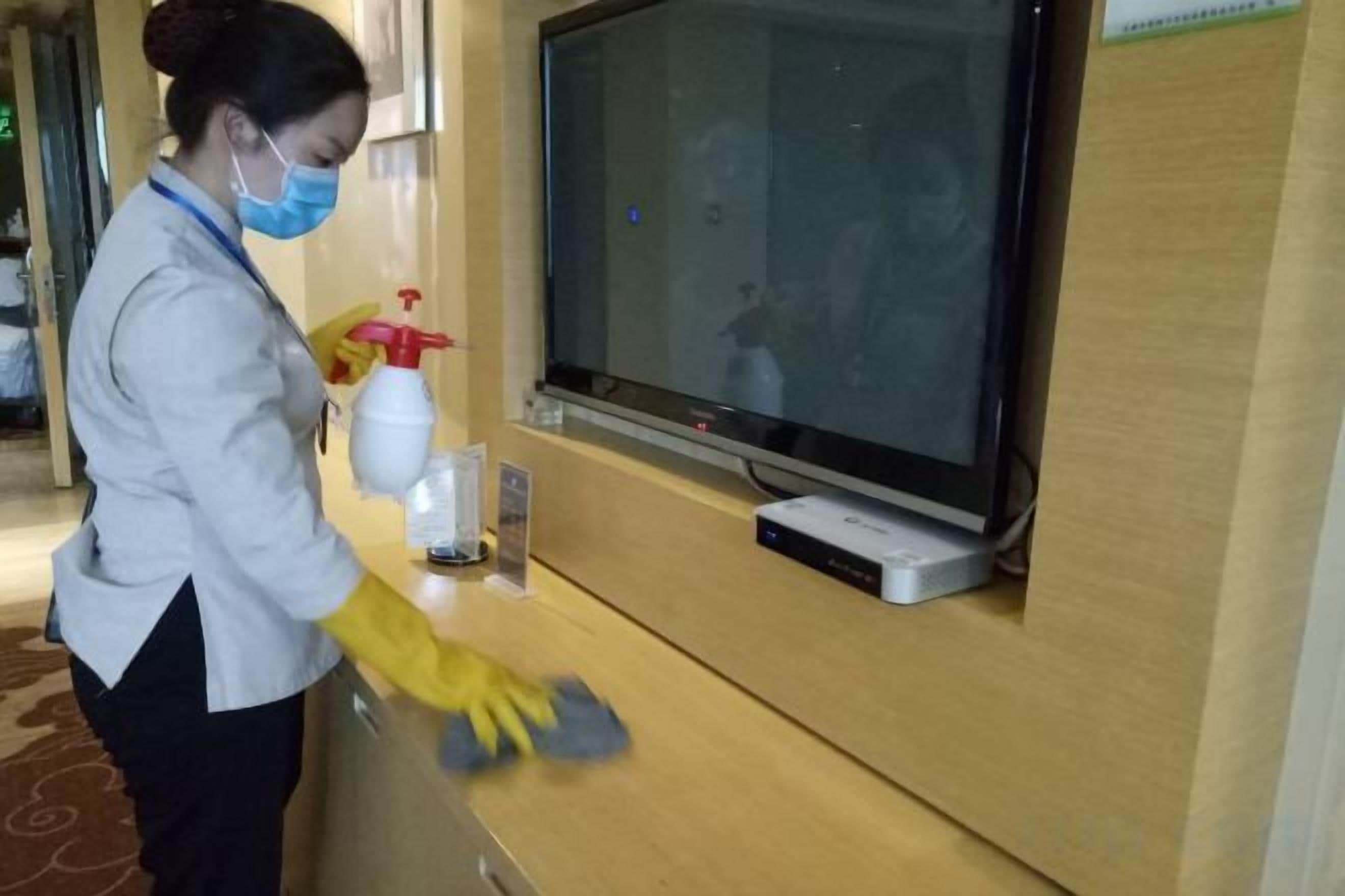Una persona limpiando un mostrador de recepción de madera con un atomizador y un paño.