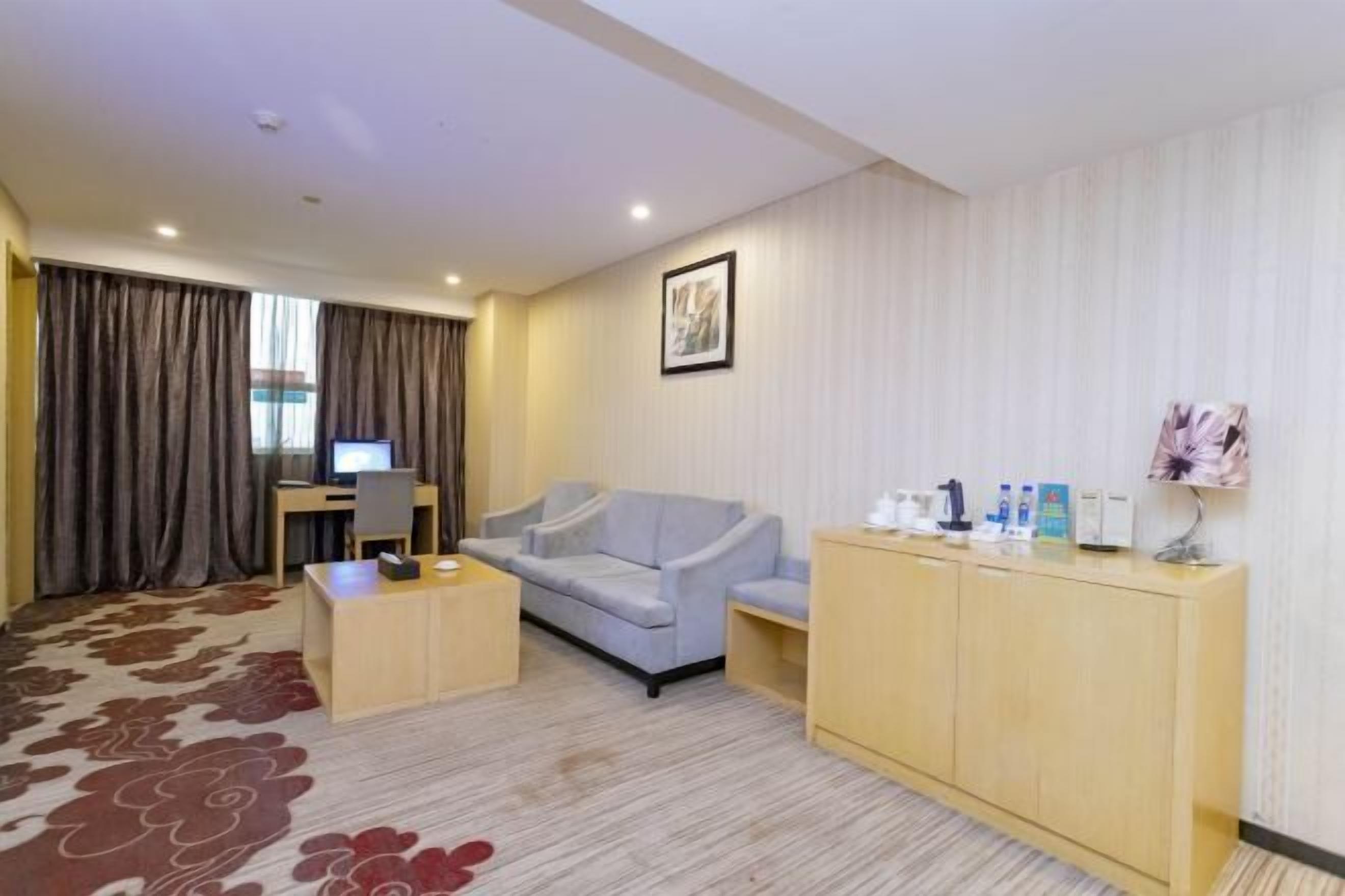 Une chambre d’hôtel avec un canapé, un bureau avec un ordinateur, une petite armoire contenant des articles de toilette et une moquette à motifs.
