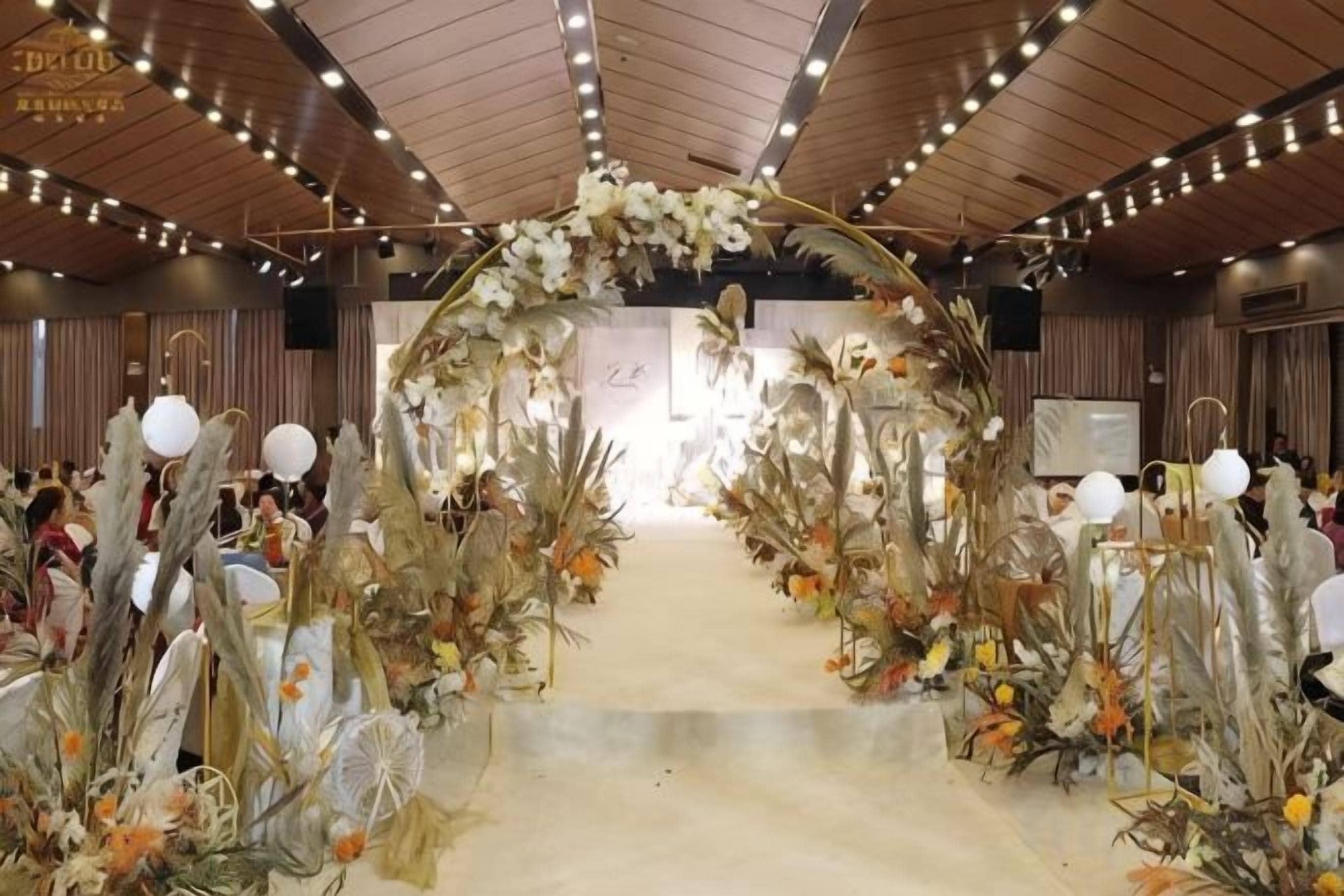 Un espace intérieur agrémenté d’une arche fleurie, d’une scène et d’un espace réservé aux spectateurs.